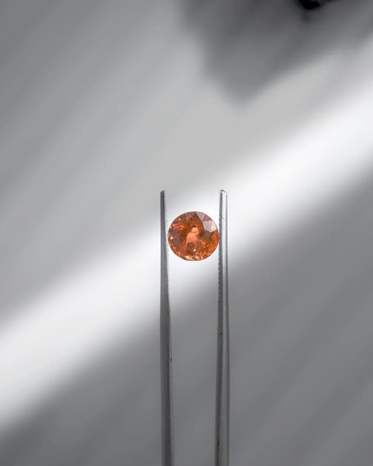 Faceted orange gemstone held by tweezers, showcasing brilliance and elegance for fine jewelry.