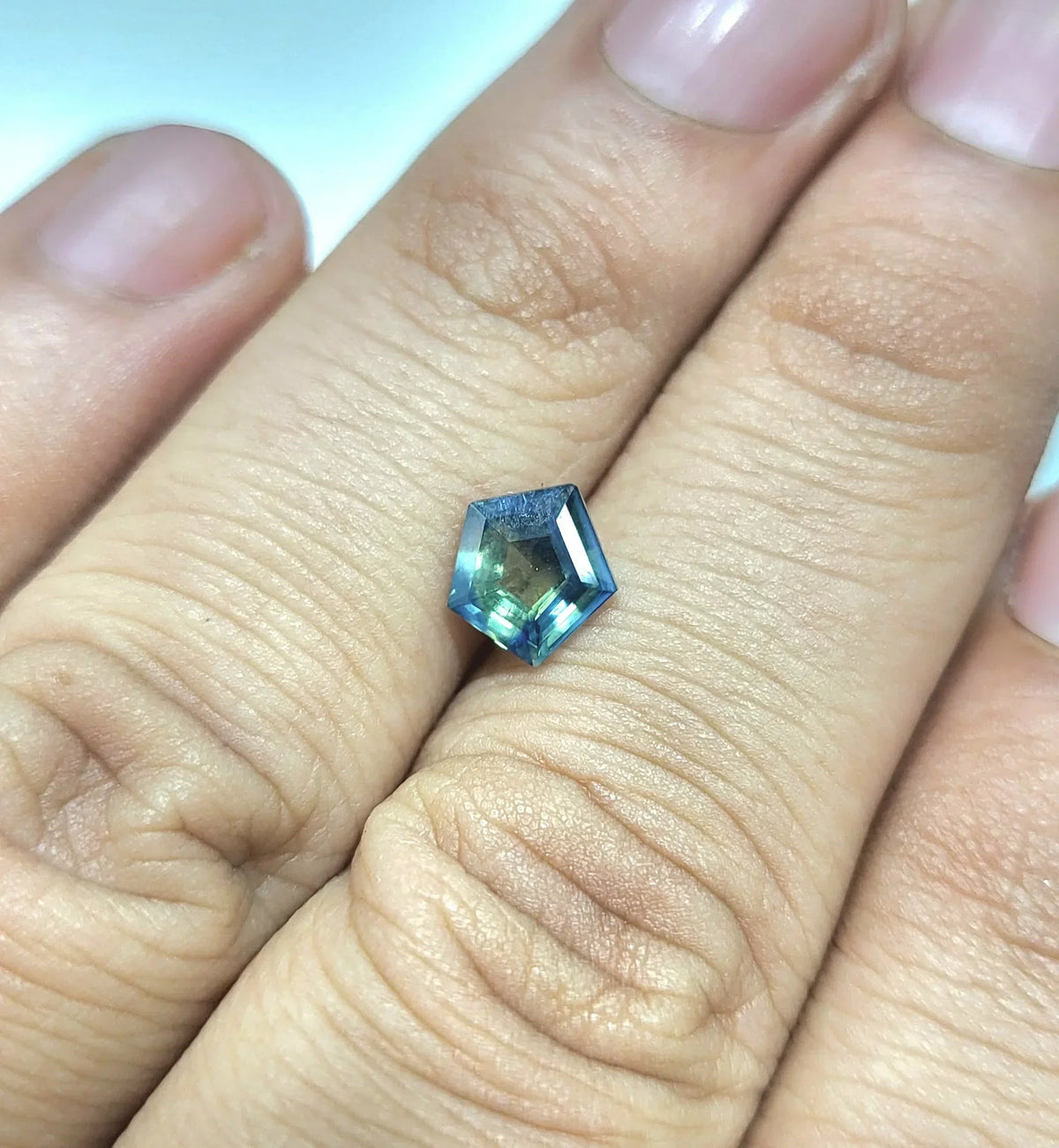Faceted blue-green gemstone held in hand, showcasing brilliance and elegance for jewelry design