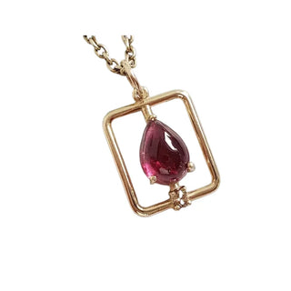 Elegant gold pendant with pear-shaped red gemstone, modern geometric frame, luxury jewelry design