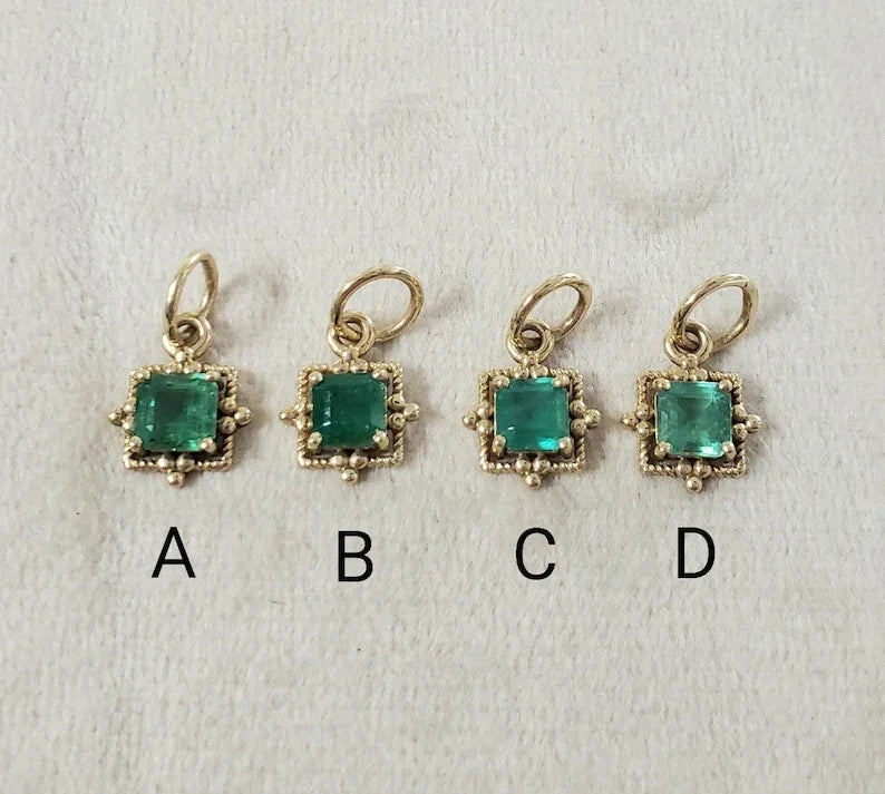 Four gold emerald charms with square-cut stones, labeled A-D, displayed on white background
