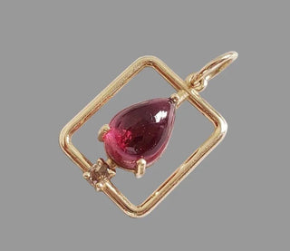 Elegant gold pendant with pear-shaped red gemstone and diamond accent, perfect for luxury jewelry lovers