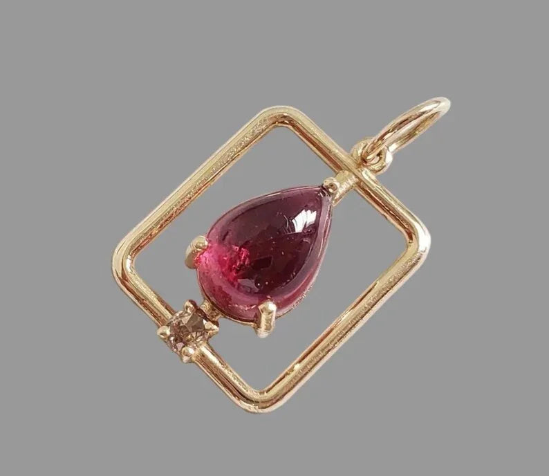 Elegant gold pendant with pear-shaped red gemstone and diamond accent, perfect for luxury jewelry lovers