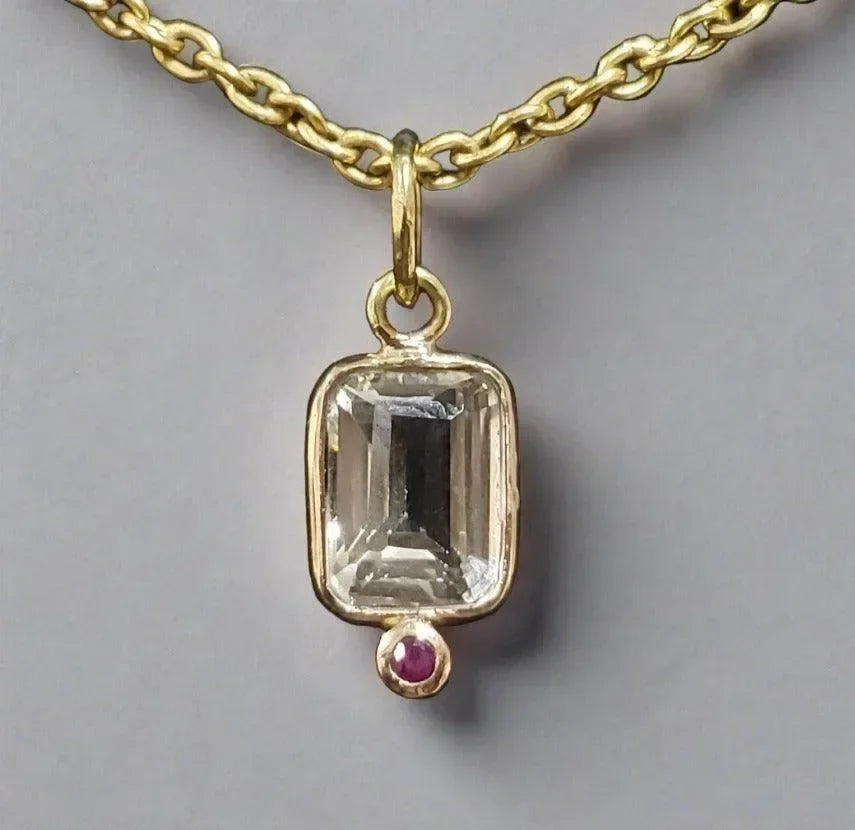 Elegant gold necklace with emerald-cut gemstone pendant and ruby accent, showcasing fine jewelry craftsmanship