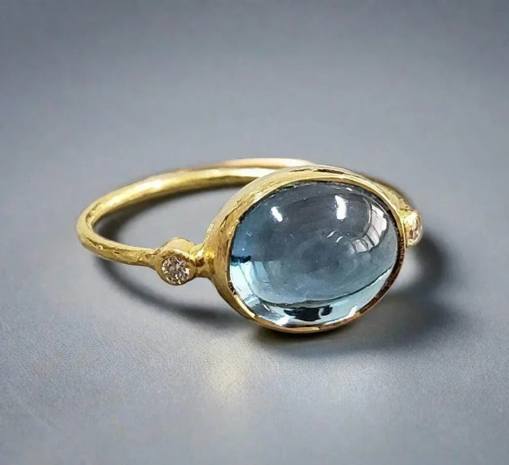 Elegant gold ring with oval blue gemstone and diamond accents, perfect for sophisticated jewelry lovers.