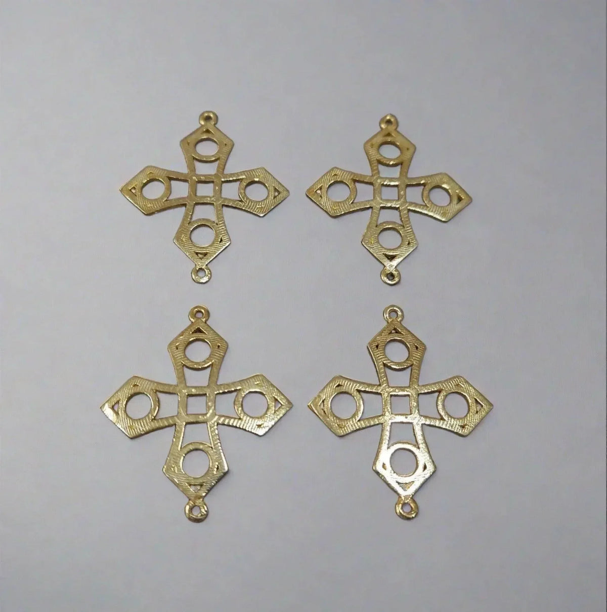 Four gold cross pendants with intricate cutout designs, ideal for elegant jewelry making