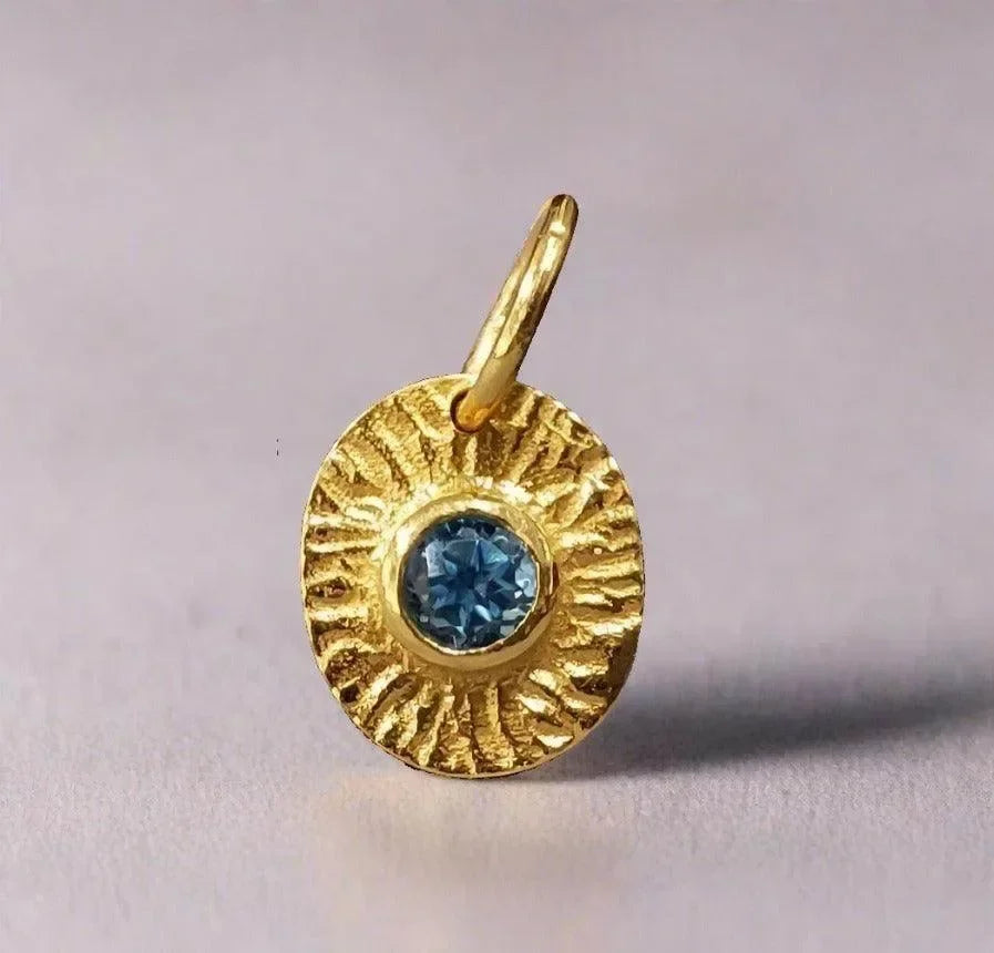 Gold pendant with blue gemstone, textured sunburst design, elegant jewelry accessory