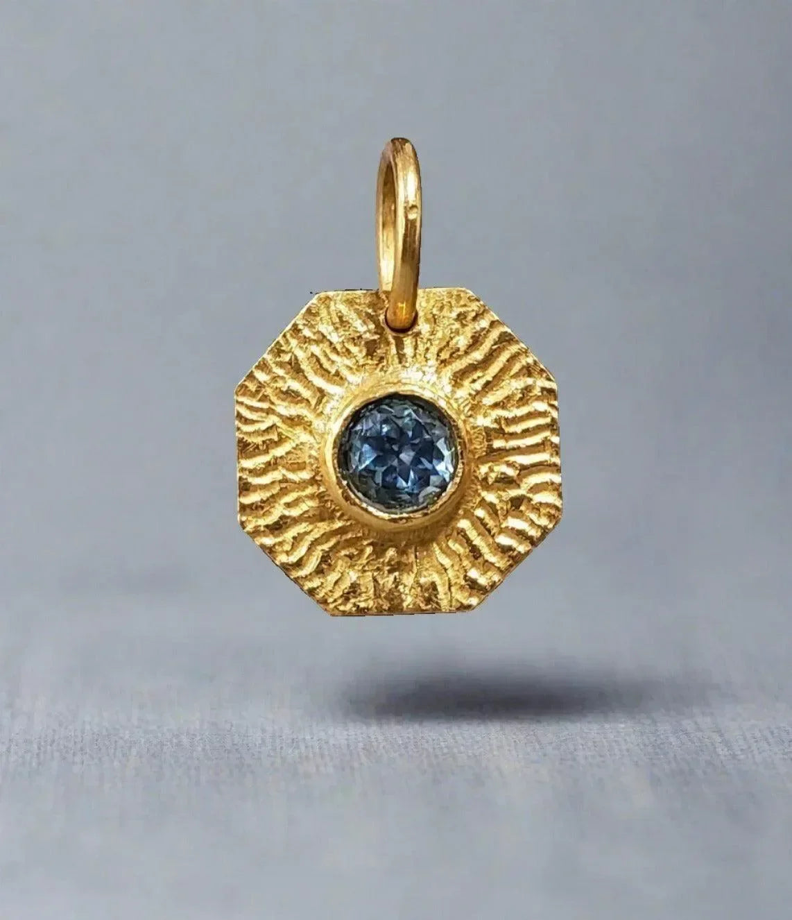 Gold octagon pendant with blue diamond, textured sunburst design, elegant jewelry accessory