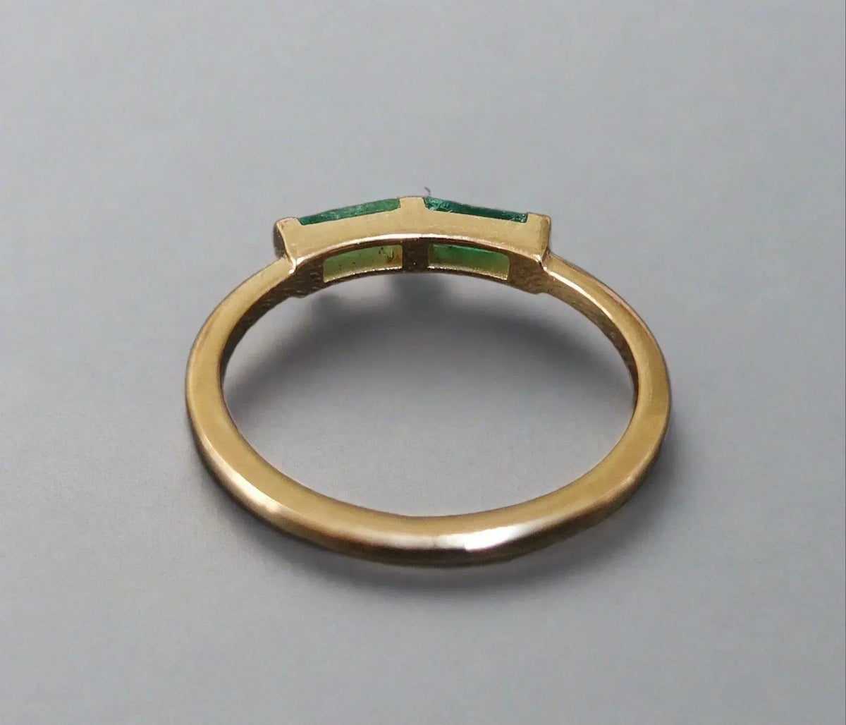 Elegant gold ring with emerald green gemstones, showcasing sophistication and timeless design.