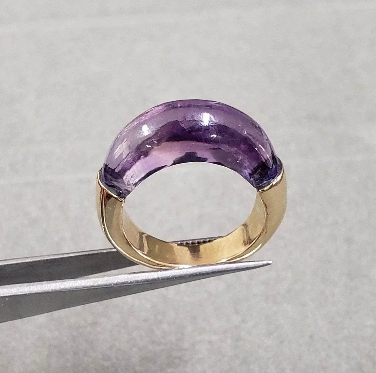 Elegant gold ring with large purple amethyst gemstone, held by tweezers for display