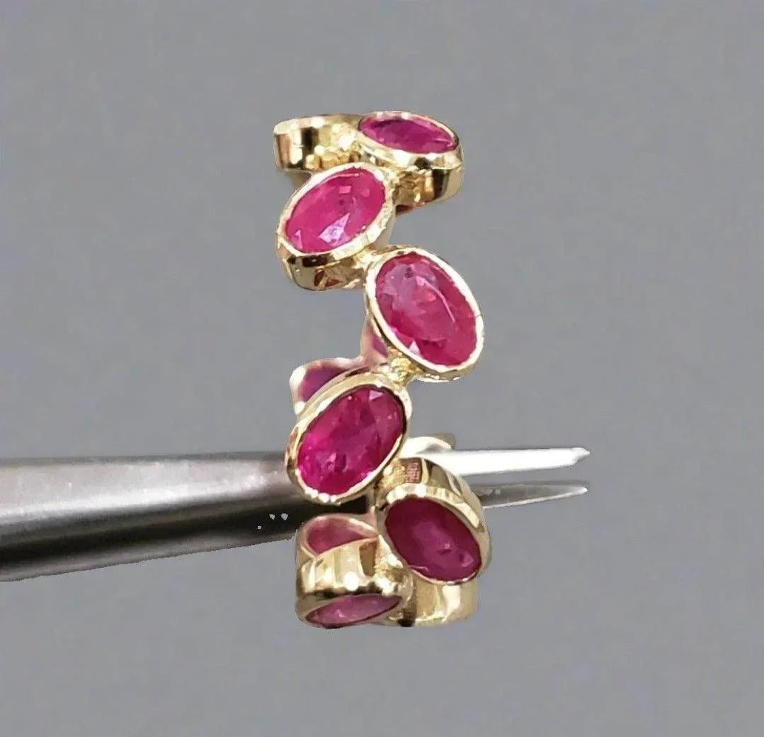 Elegant gold ring with vibrant oval rubies, held by tweezers against neutral background